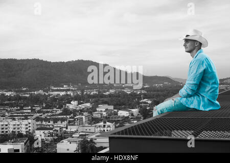 Young handsome man sitting on the roof and looking at the city Stock Photo