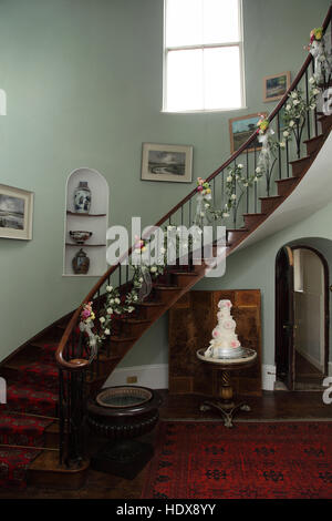 Wooden spiral staircase decorated for a wedding ceremony with flower arrangements, wedding cake on a stand. Stock Photo