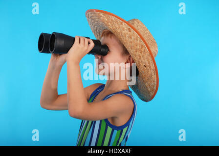 Curious boy in cowboy hat looking through binoculars. Photo on a blue background Stock Photo