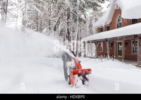 Man with a snow blower clearing a driveway in a beautiful snowy wintertime scenery of Muskoka, Ontario, Canada Stock Photo