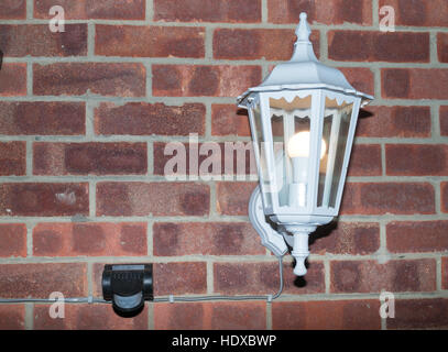Outdoor lantern with LED bulb controlled by PIR motion sensor mounted on an external brick wall. Stock Photo
