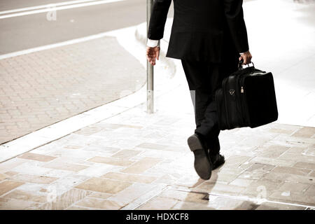 Business man in a suit holding briefcase walking down street Stock Photo
