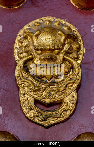 Gold Chinese lion door knocker on red door, close up of lion with ring in mouth, at Temple of Heaven in Beijing, China. Stock Photo