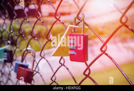 Old and rusty red padlock hanging on metal fence Stock Photo