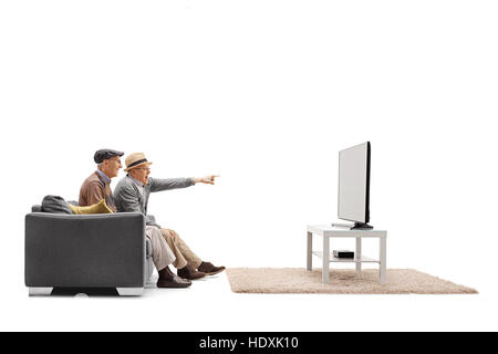 Two mature men sitting on a sofa and watching television with one of them pointing with his finger isolated on white background Stock Photo