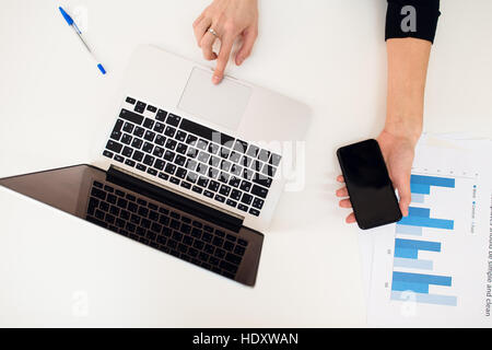 Laptop with women hand and paper graph on white table. Stock Photo