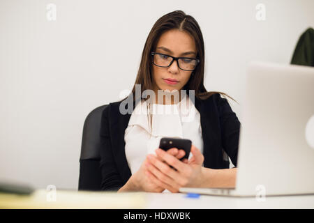 Good business talk. Cheerful young beautiful woman in glasses talking on mobile phone and using laptop with smile while sitting at her working place Stock Photo