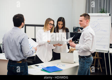Young business people sitting in office during meeting and discussing with paperwork using laptops Stock Photo