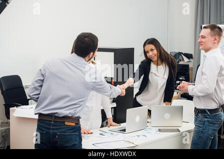 Welcome on board. Four business people sitting at the table while two of them shaking hands and smiling Stock Photo