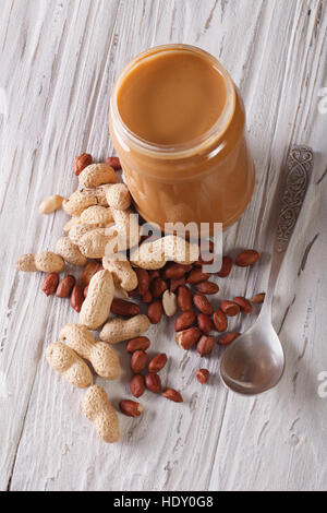 nut butters in a glass jar and peanuts close-up on an old table. vertical top view Stock Photo