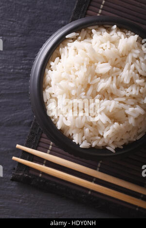 White rice in a black bowl close-up and chopsticks. vertical top view Stock Photo