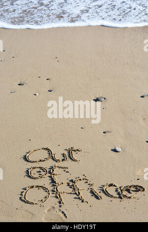 Out of office text written in sand on a beach suggesting work life balance Stock Photo