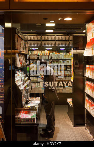 A Japanese salaryman uses a smartphone inside Tsutaya bookshop. Roppongi, Tokyo, Japan. Stock Photo