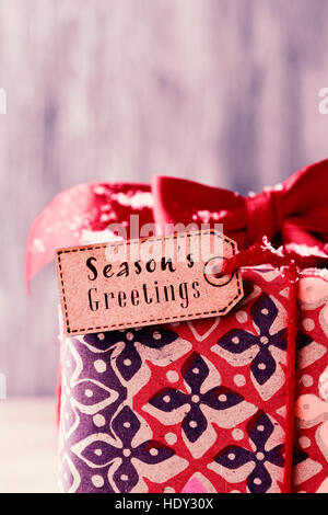 closeup of a gift topped with a red ribbon bow and with a paper label with the text seasons greetings tied to it with a red string Stock Photo