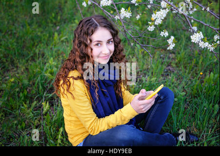 beautiful young woman sitting on the grass with phone