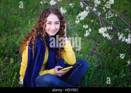 beautiful young woman sitting on the grass with phone
