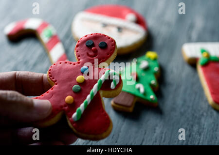 closeup of a young caucasian man with a gingerbread man in his hand and some other of christmas cookies with different shapes and colors on a rustic w Stock Photo