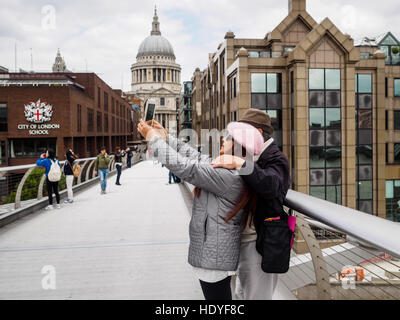 Couple using a tablet to take a selfie on the Millennium Bridge, London, England. Stock Photo