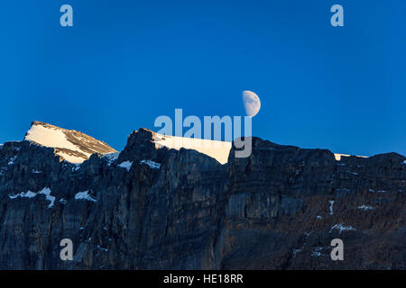 A half moon rises in a clear blue sky over a mountain range in Banff National Park in Alberta Canada. Stock Photo