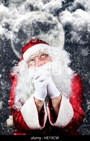 Santa Claus in the Christmas Night Praying, with Sky full of Stars, Clouds and The Moon in the Background Stock Photo