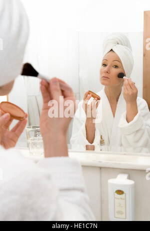 Young woman in bathroom applying, putting on blush, blusher, rouge Stock Photo