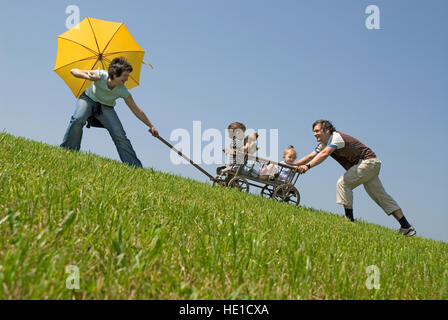 Family, couple pulling and pushing their children on a cart, toy wagon Stock Photo