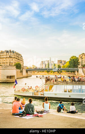 young people having a picnic on the banks of river seine at dusk Stock Photo