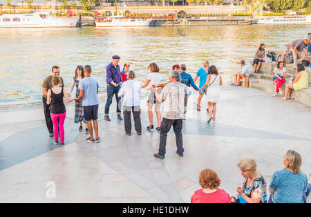 people practicing folk-dances on the banks of river seine Stock Photo