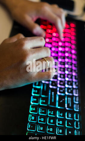 Closeup of male hands typing on colorful illuminated keyboard at night Stock Photo