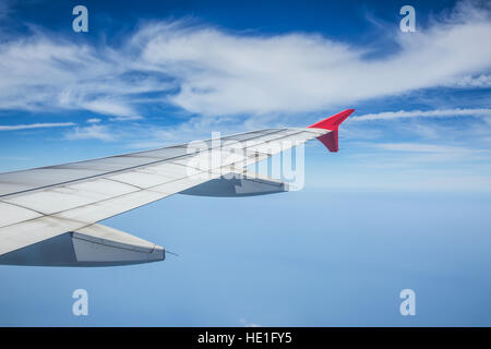 Wing of airplane flying above the clouds in the blue sky. Stock Photo