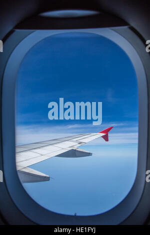 View from window of an airplane wing aircraft flying above the clouds in a blue sky. Stock Photo