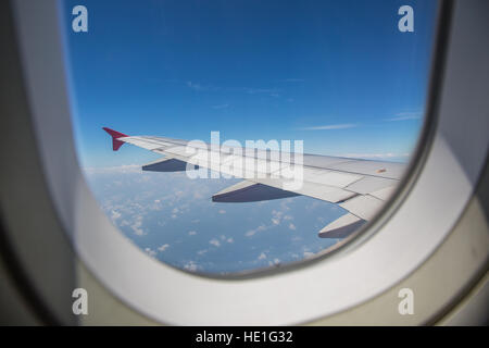 View through a window of an left airplane wing aircraft flying above the clouds with blue sky as travel by airplane concept. Stock Photo