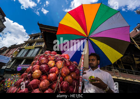 A fruit seller, using a bicycle, is offering apples on Indra Chowk in front of Akash Bhairab temple, shaded by a colorful umbrella Stock Photo