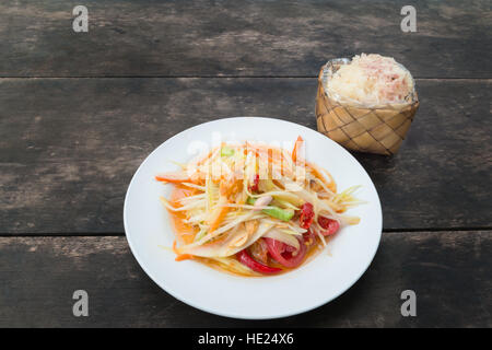 Som tam thai or Green papaya salad with sticky rice in bamboo container on wooden table at restaurant. Stock Photo