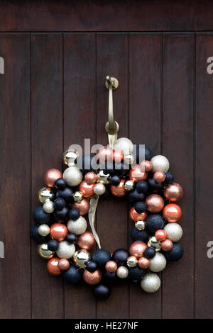 Decorative Christmas wreath hanging on a dark front door. Stock Photo