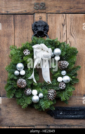 Decorative Christmas wreath hanging on a dark front door. Stock Photo