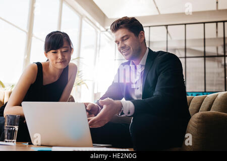 Shot of two young businesspeople using laptop in lobby of modern office. Man and woman sitting on foyer working together on laptop. Stock Photo
