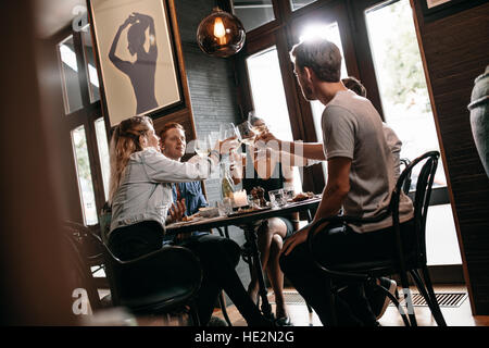 Group of friends toasting wine at restaurant. Young man and woman sitting at table and toasting drinks at cafe. Stock Photo