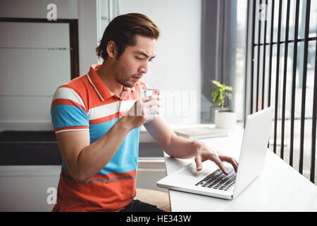 Man using laptop while drinking water in coffee shop Stock Photo
