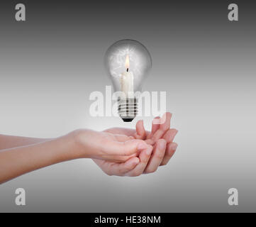 On hands levitates a broken bulb, inside there is a candle, with the flame lit, in front of a dark gray background Stock Photo