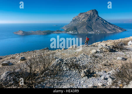 Telendos Island from Myrties, Kalymnos, blue, with evidence of fire damage in foreground and female hiker with red rucksack Stock Photo