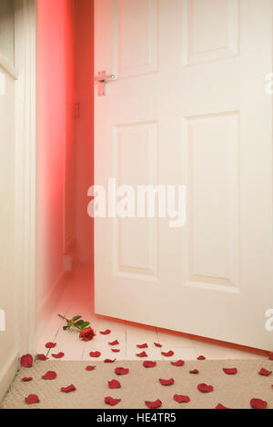 Slightly opened bedroom door with red light coming through and a red rose with rose petals scattered on the carpet floor, Stock Photo