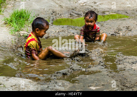 Two local boys, only wearing shirts, are playing in the mud of a waterhole Stock Photo