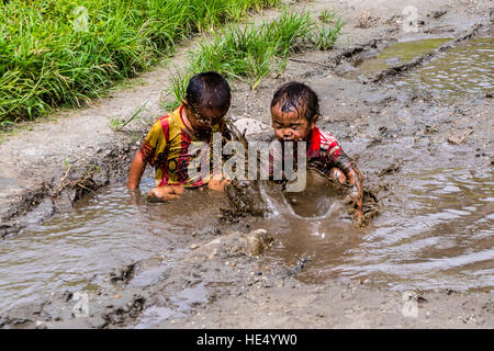 Two local boys, only wearing shirts, are playing in the mud of a waterhole Stock Photo