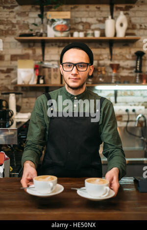 Waiter in black apron holds two cups of coffee Stock Photo