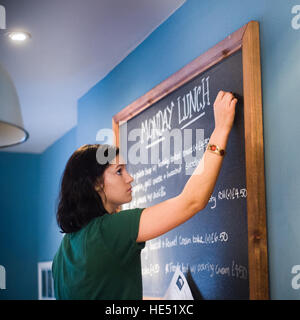 Waitress writing lunch menu on the blackboard in a cafe Stock Photo