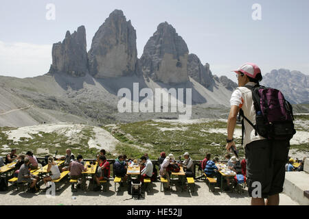 Tourists taking a break on the terrace of the Dreizinnenhuette mountain hut in front of the Tre Cime di Lavaredo Mountains or Stock Photo