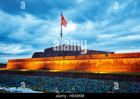 National flag of Vietnam flowing on top of the Flag Tower in the Imperial City at dusk. Hue, Vietnam. Stock Photo