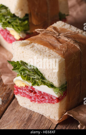 delicious homemade sandwich with salami and egg wrapped in paper close-up on the table. vertical Stock Photo