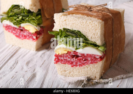 sandwiches with salami and egg wrapped in paper close-up on the table. horizontal Stock Photo